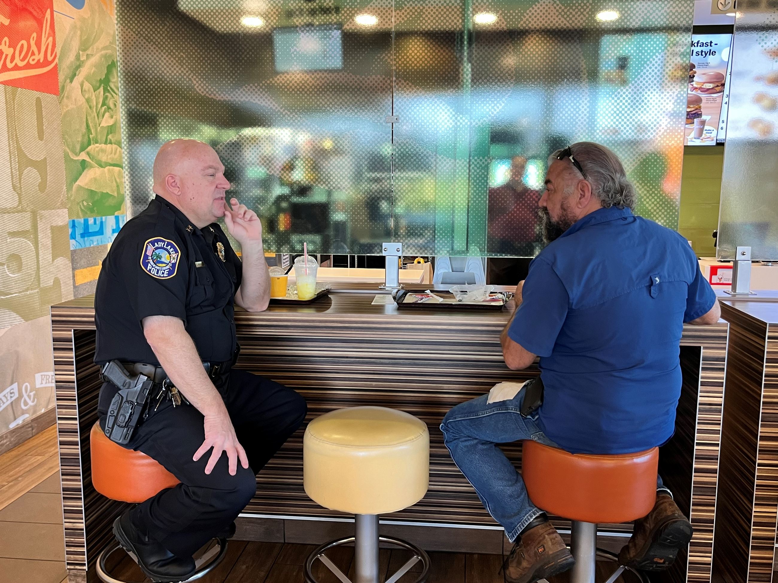 A uniformed officer sits and chats with a resident at McDonalds